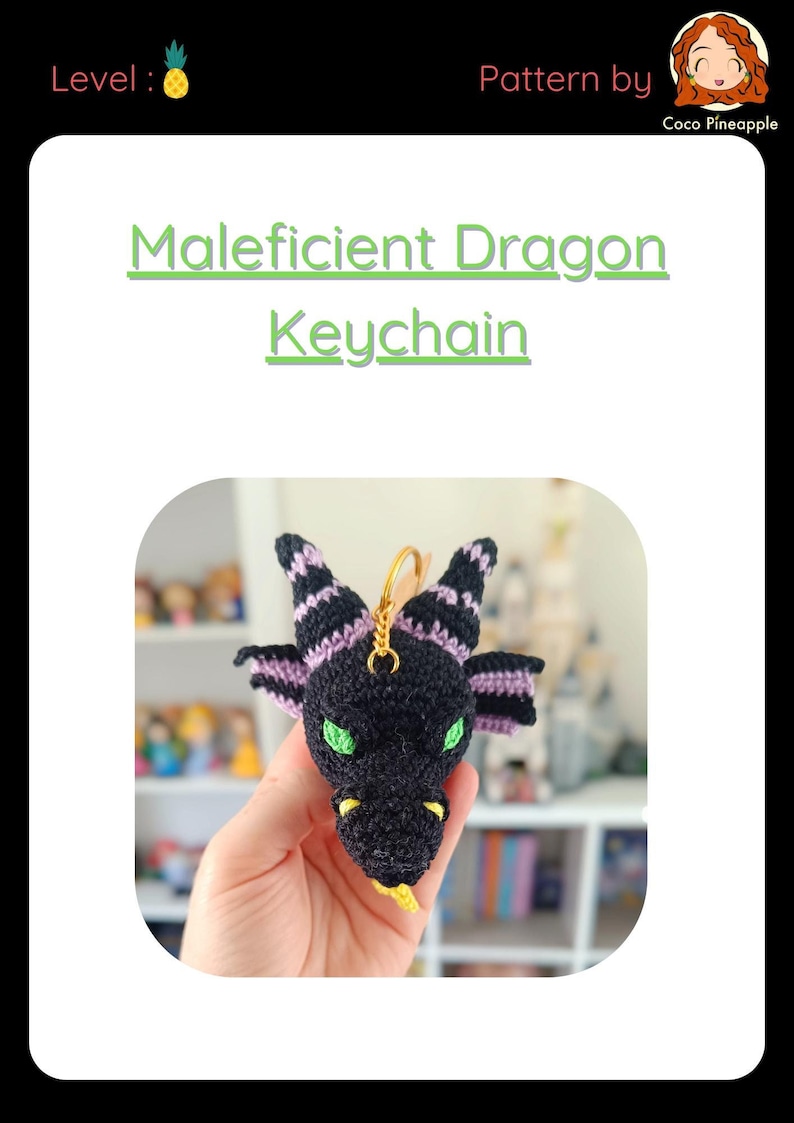 Puede incluir: Un llavero de drag&oacute;n de crochet negro y morado con ojos verdes y lengua amarilla. El llavero est&aacute; colgado de una cadena dorada.