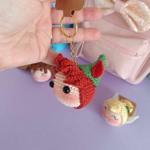 May include: Crocheted Peter Pan and Tinkerbell keychains. Peter Pan is red, green, and brown. Tinkerbell is yellow, green, and pink. Both have black eyes and are attached to gold key rings.