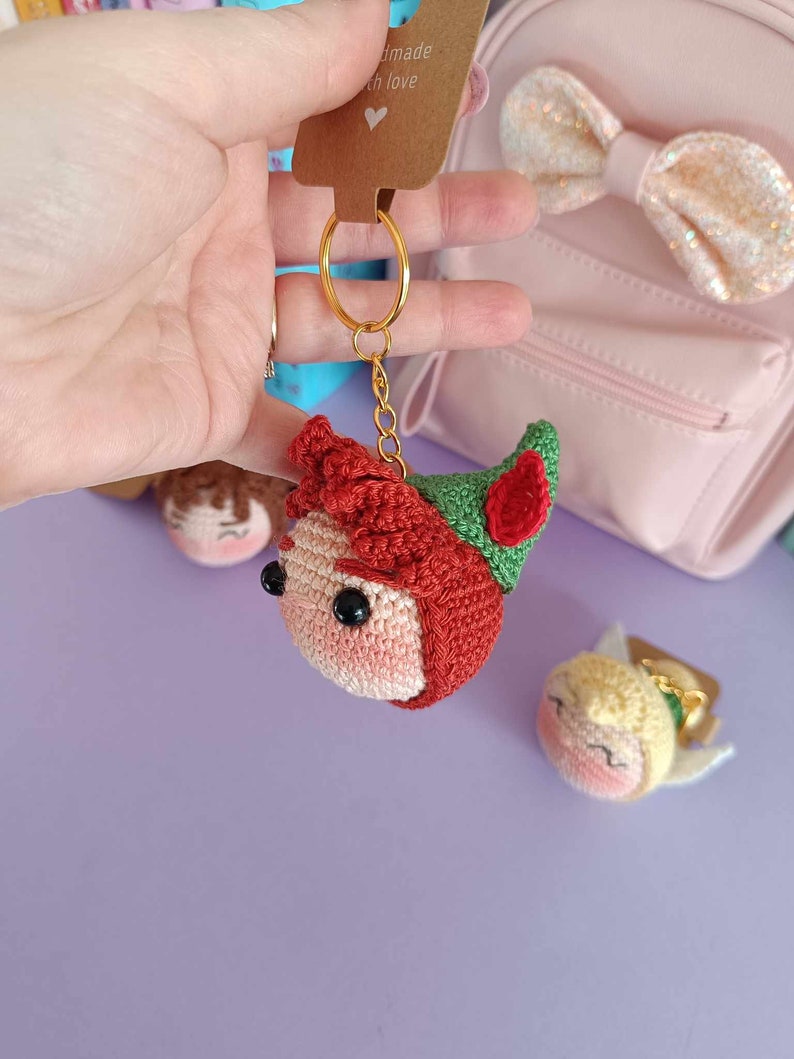 May include: Crocheted Peter Pan and Tinkerbell keychains. Peter Pan is red, green, and brown. Tinkerbell is yellow, green, and pink. Both have black eyes and are attached to gold key rings.