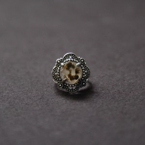 May include: A silver ring with a white and brown stone set in a decorative floral design.