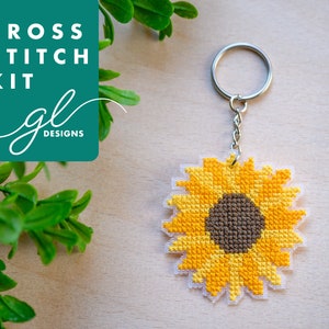 May include: Cross stitch kit for a sunflower keyring. The kit includes pre-printed fabric, embroidery floss, and a metal key ring. The finished keyring features a yellow sunflower with a brown centre.