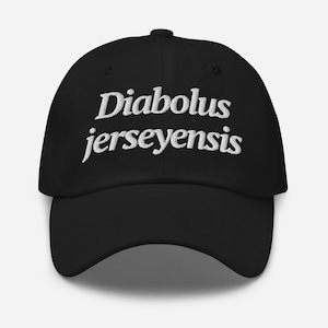 May include: A black baseball cap featuring white embroidered text on the front that reads Diabolus jerseyensis. The cap has a structured crown, a curved brim, and a button at the top center, constructed from a solid black fabric material.