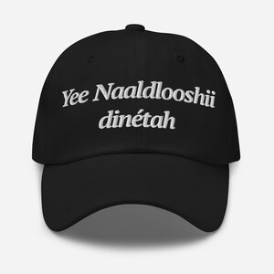 以下が含まれることがあります： フロントパネルにYee Naaldlooshii dinétahと白い刺繍が施された黒い野球帽。この帽子は構造化されたクラウン、カーブしたつば、そして中央上部にボタンを備えており、ヘッドウェアとしてクラシックな外観を提供しています。