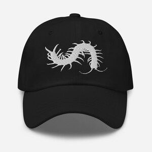 Peut inclure: Une casquette de baseball noire avec une broderie blanche représentant un mille-pattes centrée sur le panneau avant. La casquette présente une calotte structurée, une visière incurvée et un bouton sur le dessus, avec un motif cousu détaillé.