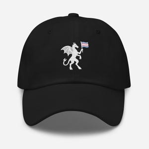 May include: A black baseball cap featuring an embroidered white dragon graphic on the front. The dragon is depicted in a stylized line-art pattern and is holding a small flag with horizontal light blue, pink, and white stripes in its claw.
