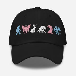 May include: A black baseball cap featuring an embroidered row of six mythical creatures in light blue and pink thread. The design includes a sasquatch, mothman, jackalope, werewolf, sandworm, and dragon, all rendered in a striped, textured style.