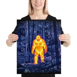 May include: A rectangular poster featuring a thermal imaging style graphic of a large, hairy, bipedal creature standing in a dark forest. The creature is rendered in bright yellow, orange, and red hues, contrasting against the deep blue forest background.