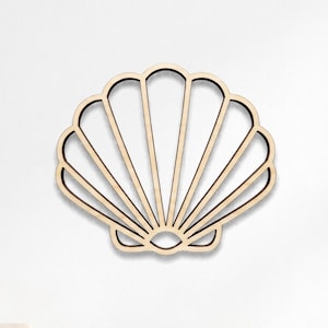 May include: A light-coloured wooden wall cutout in the shape of a scallop shell with a symmetrical, open-frame design featuring radiating lines and a curved bottom edge, mounted on a plain white wall above a white storage unit with various items.