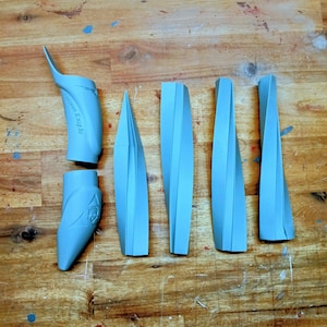 Könnte beinhalten: Eine Ansammlung hellblauer 3D-gedruckter Teile, darunter gebogene und eckige Formen, angeordnet auf einer Holzoberfläche. Einige Teile tragen den Text "Goteam Knight". Die Teile scheinen Komponenten eines größeren Objekts zu sein.