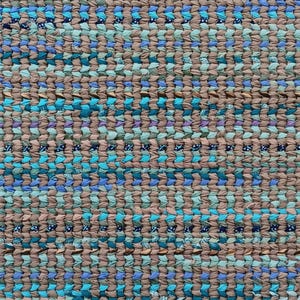 May include: A rectangular woven rug featuring a dense, textured pattern of interlaced fabric strips. The color palette consists of alternating horizontal bands of neutral taupe, various shades of bright blue, teal, and dark navy accents.