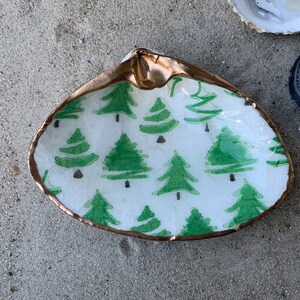 May include: A white seashell with a gold rim and a green Christmas tree pattern. The shell is a decorative dish.