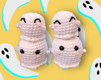 May include: Two handmade, white crochet ghost figures with black button eyes and smiling faces with pink cheeks. The ghosts are stacked, with a smaller head on top of a larger body. The background is yellow with white ghost illustrations.