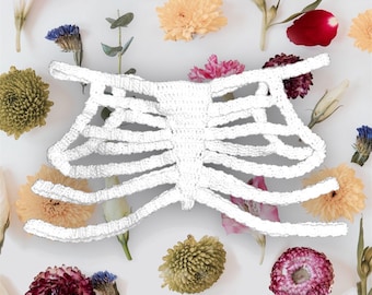 May include: White crocheted rib cage costume. The rib cage is made of white yarn and is crocheted in a delicate pattern. The rib cage is surrounded by dried flowers.