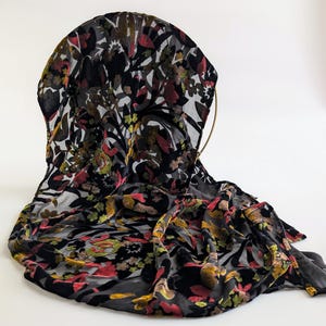 May include: A black sheer scarf with a floral pattern in shades of red, yellow, and green. The scarf is made of a soft, luxurious fabric and has a flowing, elegant drape.