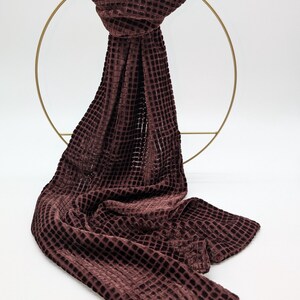 May include: A burgundy waffle-textured velvet scarf. The scarf is draped over a gold metal ring.