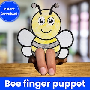 Puede incluir: Una marioneta de dedo de abeja amarilla y negra con una cara sonriente y alas blancas. La marioneta está sujeta por dedos. Las palabras "Descarga instantánea" están en un círculo azul. El texto "Bee finger puppet" está en una pancarta azul.