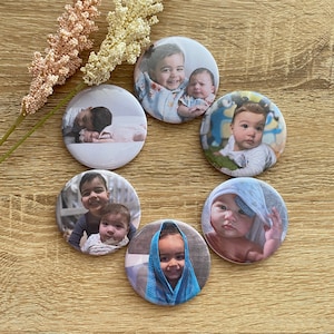 May include: Six round button badges with images of children. The badges are white with a silver border. The images are of children of different ages and ethnicities. Some of the children are smiling, while others are looking at the camera.