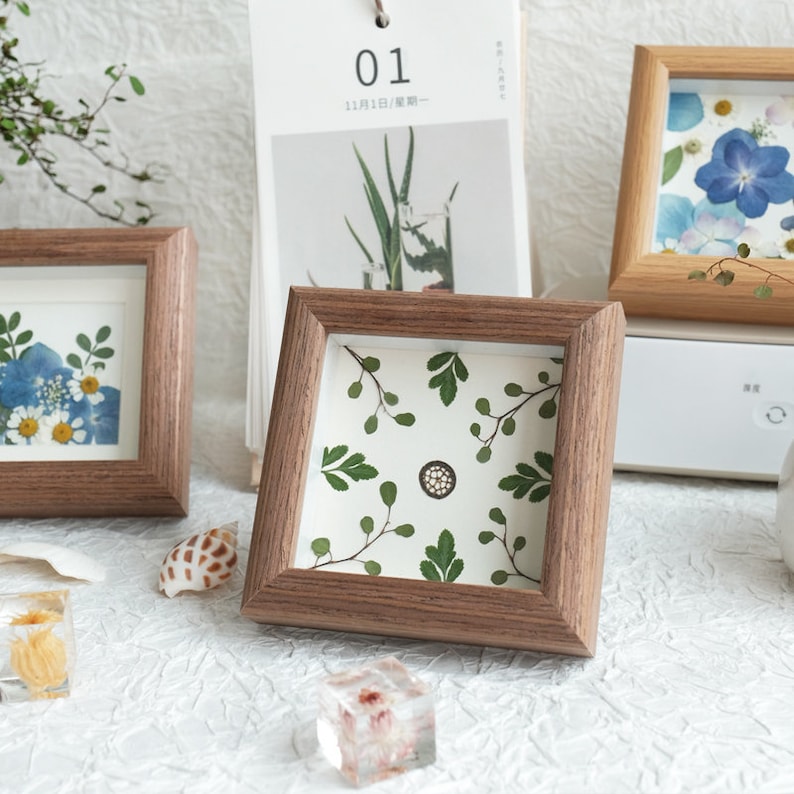 May include: Three wooden picture frames with pressed flowers and leaves inside. The frames are all different sizes and have a natural wood finish.