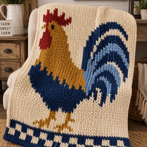 Peut inclure: Un plaid en grosse maille de couleur crème orné d'un grand motif de coq. Le coq présente une crête rouge, un corps jaune doré et une queue bleu foncé. Le bord inférieur de la couverture affiche une bordure à motif damier bleu et crème.