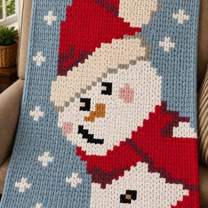 Peut inclure: Une couverture en tricot épais présentant un motif de bonhomme de neige pixélisé sur un fond bleu clair. Le bonhomme de neige porte un bonnet et une écharpe rouges, avec des flocons blancs dispersés sur le champ bleu. Aspect laine douce.