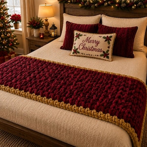 May include: A bed featuring a cream-colored quilt, two dark red velvet pillows, and a rectangular accent pillow with the text Merry Christmas and holly leaves. A chunky knit dark red bed runner with gold braided trim lies across the foot.
