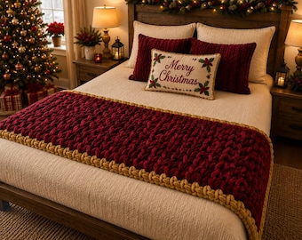 May include: A bed featuring a cream-colored quilt, two dark red velvet pillows, and a rectangular accent pillow with the text Merry Christmas and holly leaves. A chunky knit dark red bed runner with gold braided trim lies across the foot.