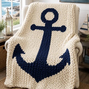 Peut inclure: Un plaid en grosse maille de couleur crème avec un grand motif d'ancre bleu marine foncé centré sur le devant. La couverture présente une construction en fil épais et texturé avec un motif en tricot torsadé sur toute la pièce.
