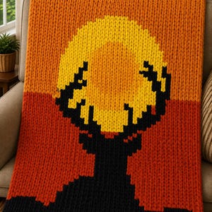 May include: A chunky knit blanket featuring a pixelated graphic of a black deer silhouette against a sunset background. The design incorporates horizontal bands of orange and dark red yarn, with a large yellow circle representing the sun.