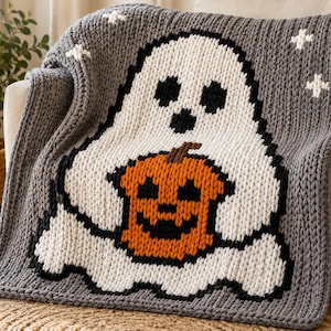 May include: A chunky knit throw blanket in gray featuring a large white ghost character with black eyes and mouth. The ghost is holding a bright orange jack-o'-lantern pumpkin with a black face. Small white cross-stitch stars accent the corners.