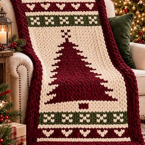 Könnte beinhalten: Eine grob gestrickte Wohndecke mit einem großen, dunkelroten Weihnachtsbaum-Motiv auf cremefarbenem Hintergrund. Die Decke hat einen dicken dunkelroten Rand sowie horizontale Bänder mit grün-cremefarbenen geometrischen Mustern oben und unten.