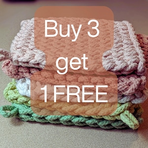 May include: A stack of handmade crochet washcloths in various colors, including pink, green, and yellow. The washcloths are made with a thick, textured yarn and have a loop for hanging. The text "Buy 3 get 1 FREE" is overlaid on the image.