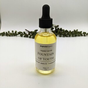 May include: A clear glass bottle with a black dropper top and a white label that reads "Brightside Organics Organic Face Oil FOUNTAIN OF YOUTH Jojoba Oil - Frankincense" and "Delray, FL 2 oz."