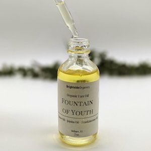 May include: A clear glass bottle with a dropper filled with a yellow liquid. The bottle has a label that reads "Brightside Organics Organic Face Oil FOUNTAIN OF YOUTH Castor Oil - Jojoba Oil - Frankincense Oil Delray, FL 2 oz."