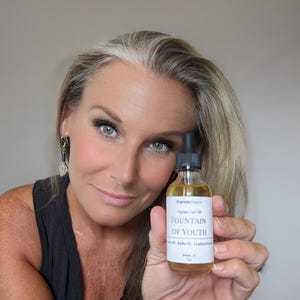 May include: A clear glass bottle with a white label that reads "Brightidea Organics Organic Face Oil Fountain of Youth Jojoba Oil | Frankincense Oil Delaware, FL 7ml".