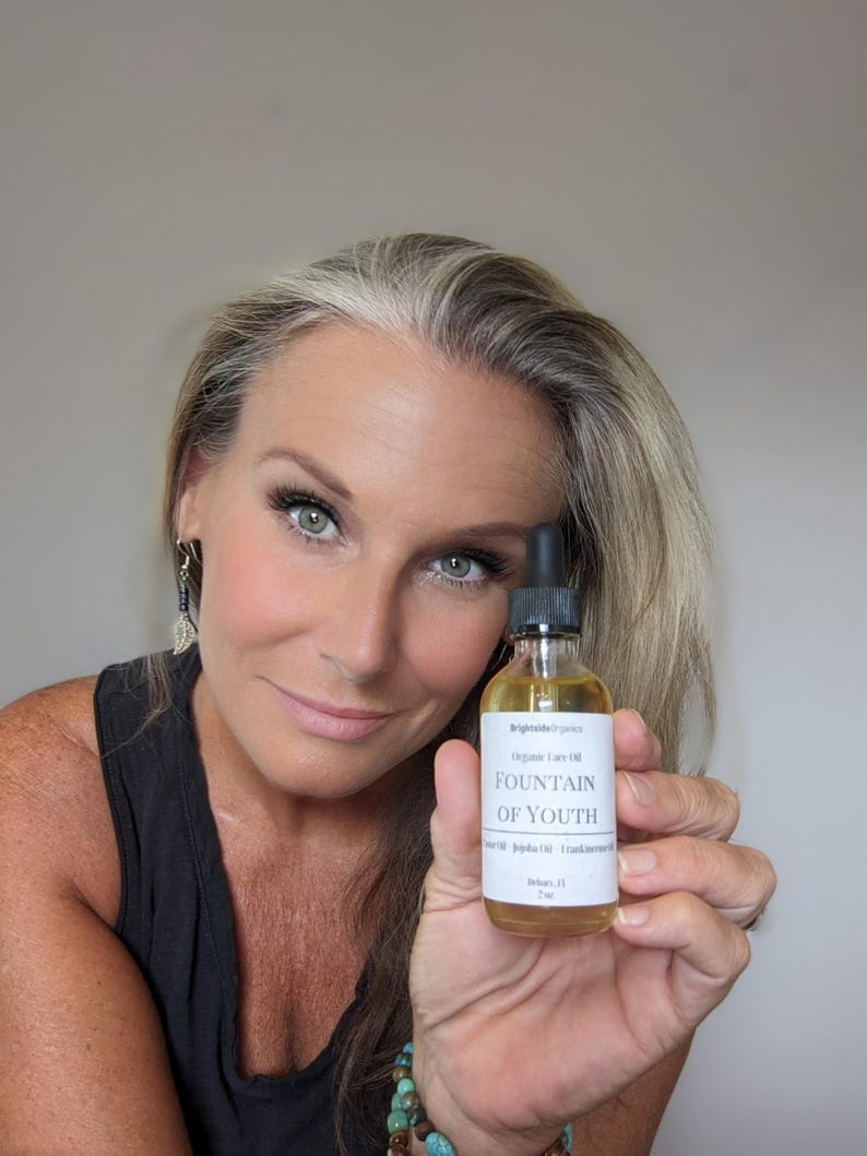 May include: A clear glass bottle with a white label that reads "Brightidea Organics Organic Face Oil Fountain of Youth Jojoba Oil | Frankincense Oil Delaware, FL 7ml".
