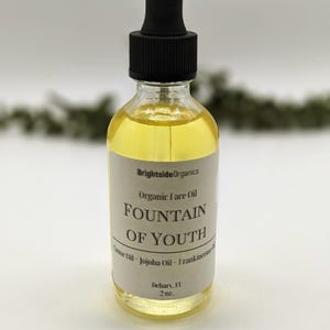 May include: A clear glass bottle with a black dropper top filled with a yellow liquid. The label reads "Brightside Organics Organic Face Oil Fountain of Youth Castor Oil - Jojoba Oil - Frankincense Oil" and "Dehors, 2 oz."