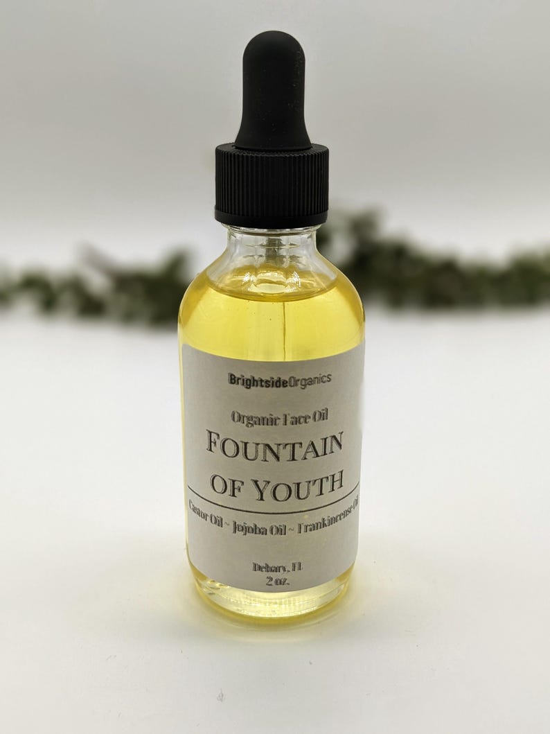 May include: A clear glass bottle with a black dropper top filled with a yellow liquid. The label reads "Brightside Organics Organic Face Oil Fountain of Youth Castor Oil - Jojoba Oil - Frankincense Oil" and "Dehors, 2 oz."
