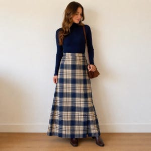 May include: A navy blue turtleneck top and a long, plaid skirt in navy, beige, and black. The skirt has a traditional tartan design and a subtle A-line cut. The ensemble is finished with brown shoes and a brown shoulder bag.