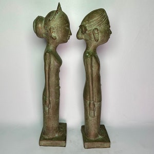 Puede incluir: Un par de estatuas de bronce verde de un hombre y una mujer de pie uno al lado del otro. Las estatuas son estilizadas y tienen rasgos exagerados. La mujer lleva un tocado tradicional y el hombre lleva un turbante.