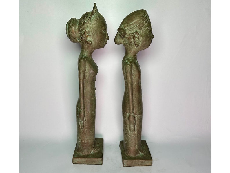 Puede incluir: Un par de estatuas de bronce verde de un hombre y una mujer de pie uno al lado del otro. Las estatuas son estilizadas y tienen rasgos exagerados. La mujer lleva un tocado tradicional y el hombre lleva un turbante.