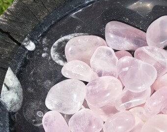 May include: A bowl filled with tumbled rose quartz stones. The stones are a light pink color and have a smooth, polished finish.
