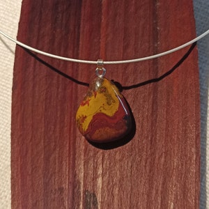 May include: A silver chain necklace with a teardrop-shaped pendant made of red, yellow, and brown jasper.