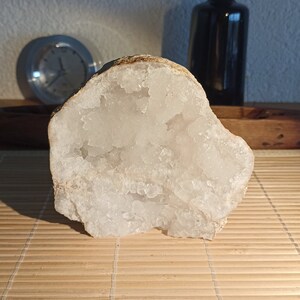May include: A large, white, geode with a rough, brown exterior. The geode is open, revealing a cavity filled with white, crystalline formations.