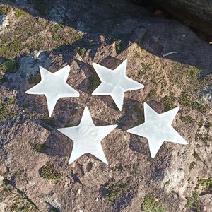 May include: Four white, frosted glass star-shaped ornaments on a gray, textured surface.