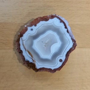 May include: A white agate slice with brown edges and intricate patterns. The agate has a natural, organic shape and a smooth, polished surface.