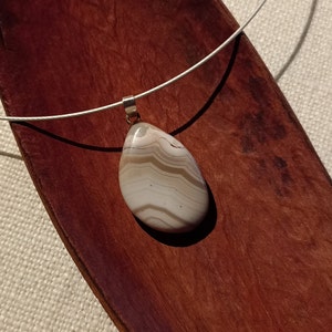 May include: A silver chain necklace with a white and brown agate pendant. The pendant is a teardrop shape with brown and white stripes.