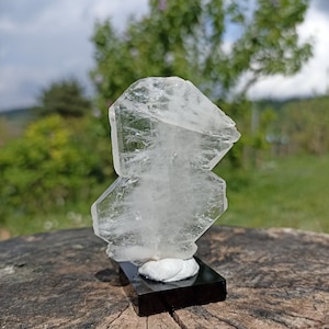 May include: A clear, faceted crystal on a black stand. The crystal is shaped like a tower and has a natural, rough texture.