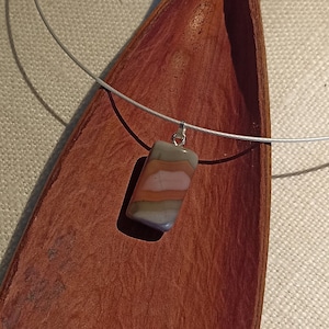 May include: A silver chain necklace with a rectangular pendant made of layered stone. The stone is a mix of brown, pink, and gray.