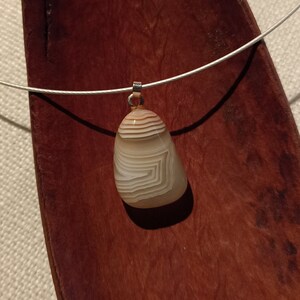 May include: A silver chain necklace with a light brown agate pendant. The pendant has a unique pattern of white and brown lines.