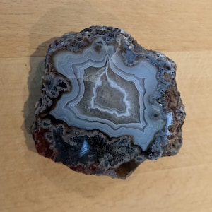 May include: A gray and white agate geode with a natural, rough exterior. The geode has a banded pattern of white, gray, and brown.